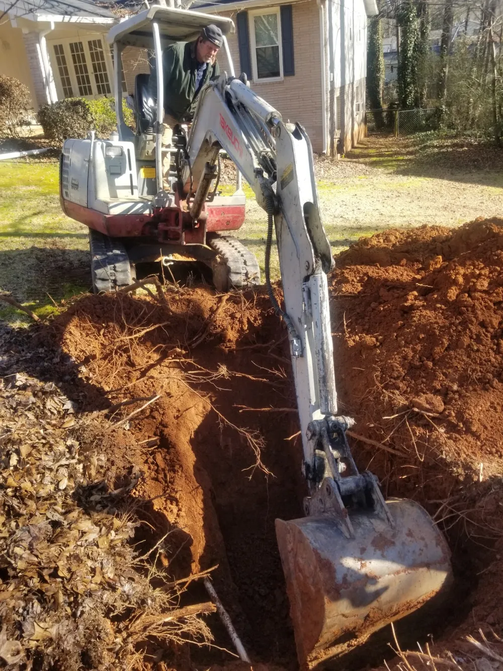 Mike's Plumbing excavator opening a trench on a residential job to reach an underground line in Stockbridge, GA